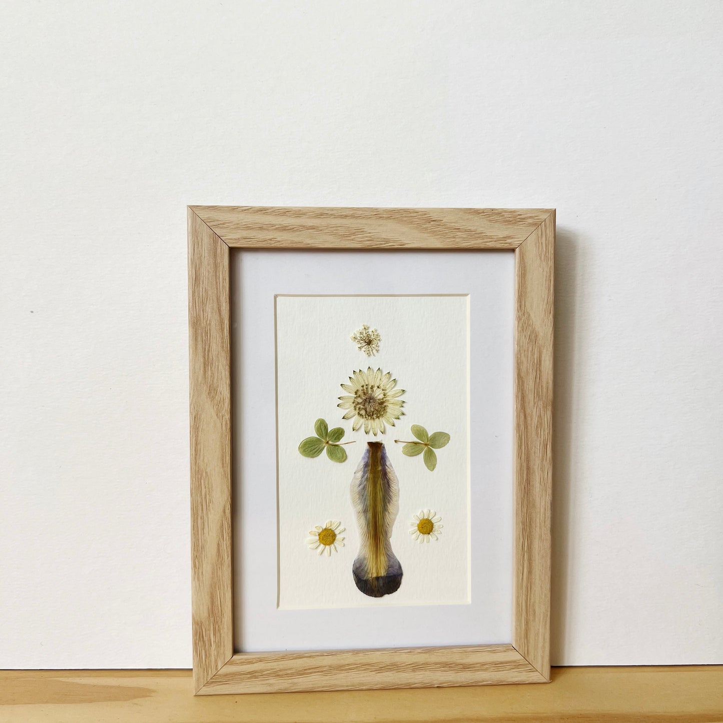 Pressed flower picture frame with Iris Hydrangea Astrantia and Margarita flowers on white background inside natural wood frame