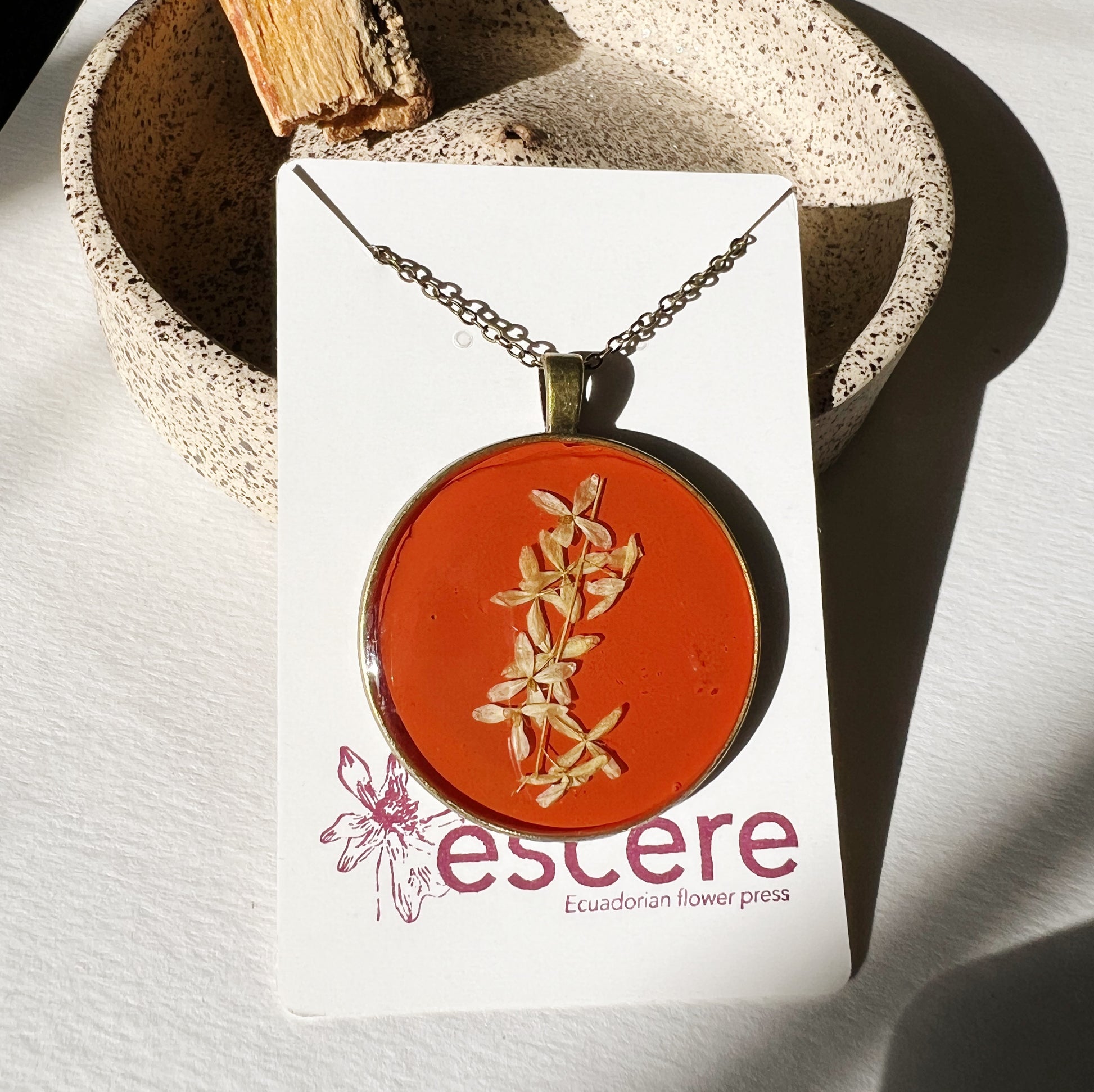 Bronze pendant necklace with pressed flowers on red orange background in epoxy resin on bronze chain