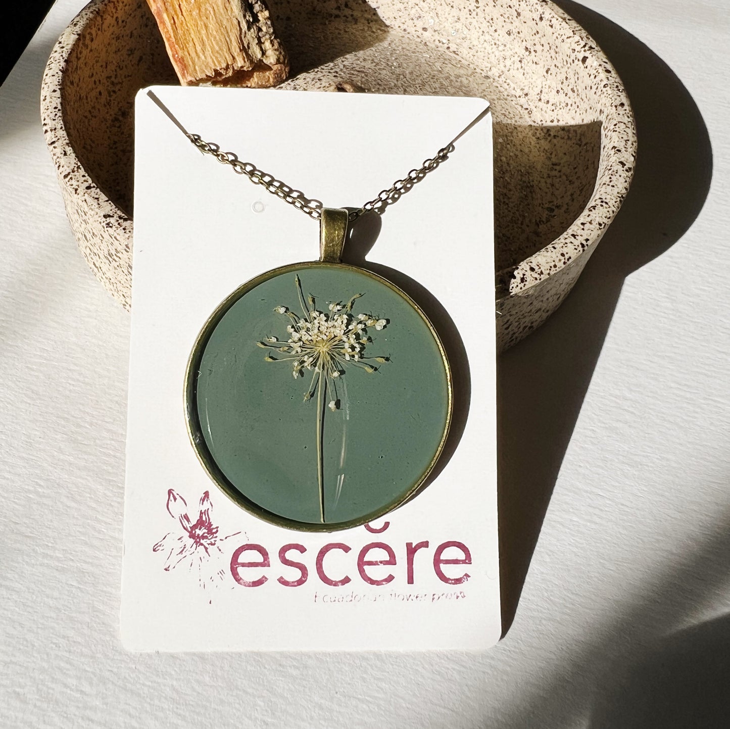 Bronze pendant necklace with pressed flowers on grey blue background in epoxy resin on bronze chain