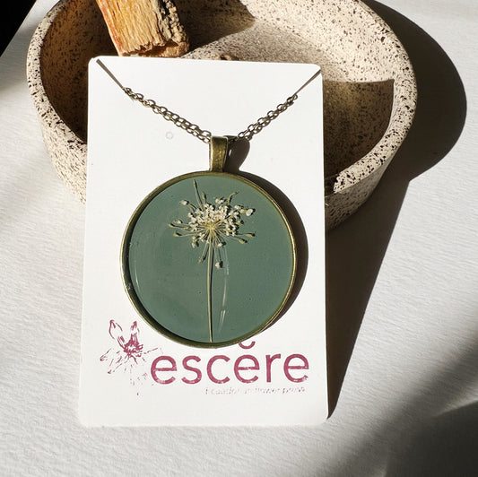 Bronze pendant necklace with pressed flowers on grey blue background in epoxy resin on bronze chain
