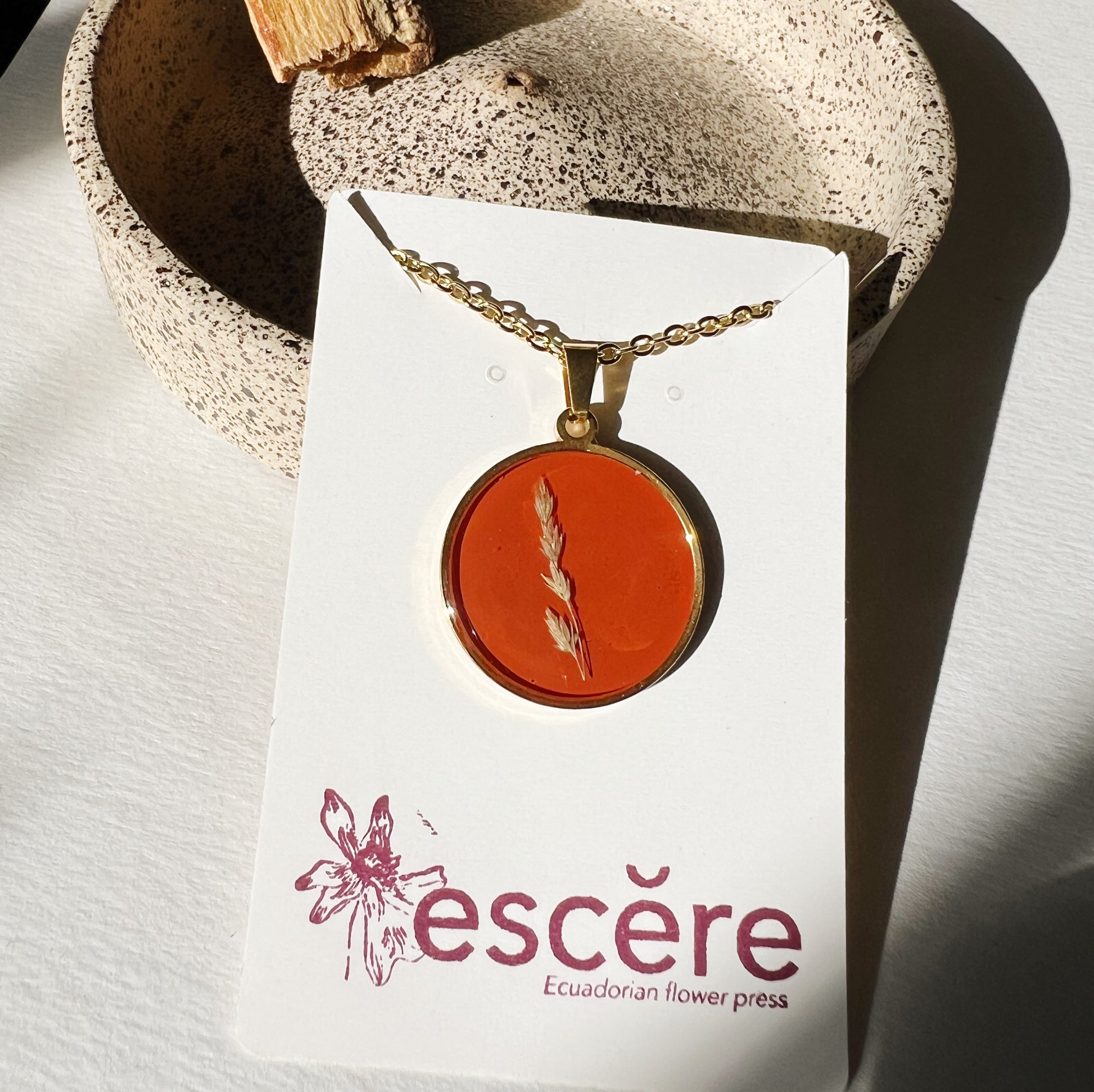 Gold pendant necklace with pressed flower grass on red orange background in epoxy resin on gold chain