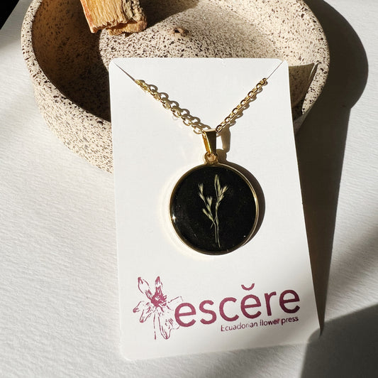 Gold pendant necklace with pressed flower grass on black background in epoxy resin on gold chain